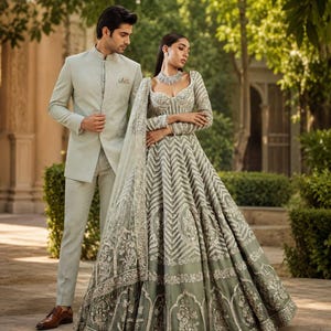 May include: A light sage green sherwani with a mandarin collar and matching trousers paired with a floor-length lehenga featuring intricate silver embroidery, a sweetheart neckline, long sleeves, and a sheer dupatta with detailed floral embellishments.