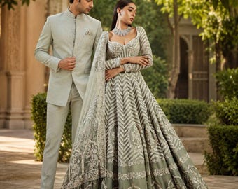 May include: A light sage green sherwani with a mandarin collar and matching trousers paired with a floor-length lehenga featuring intricate silver embroidery, a sweetheart neckline, long sleeves, and a sheer dupatta with detailed floral embellishments.