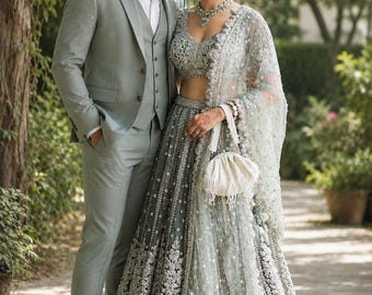 Può includere: Un completo tre pezzi verde salvia chiaro con camicia bianca e scarpe eleganti marroni, abbinato a un lehenga verde salvia con ricami argentati, dupatta coordinata, una collana di perline e una piccola borsa bianca con coulisse.