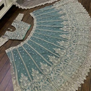 May include: A teal net lehenga with silver embroidery and a matching embroidered blouse. The lehenga has a scalloped hem and the blouse has a round neckline.