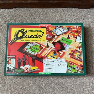 May include: A vintage Clue board game with a red, green, and yellow box. The game board is visible, along with game pieces, cards, and dice. The box features the game's title, "Original Cluedo! The Great Detective Game."