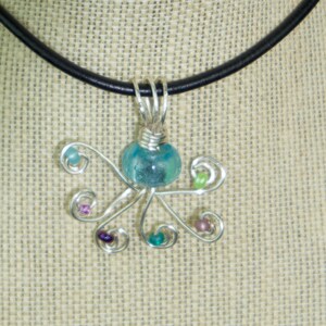 May include: A turquoise glass bead octopus pendant with silver wire and colorful beads hangs from a black leather cord necklace.