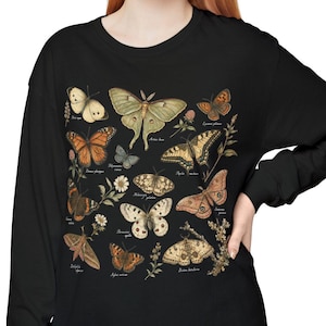 May include: A black long-sleeve shirt featuring a detailed graphic print of various moth and butterfly species in muted earth tones. Each insect is labeled with small text, and the design includes botanical elements like small flowers and sprigs.