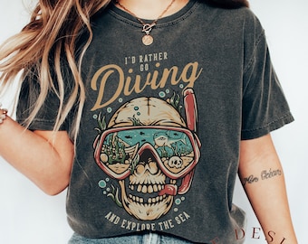 Puede incluir: Una camiseta gris oscuro con una calavera con una máscara de buceo y el texto "Prefiero ir a bucear y explorar el mar".