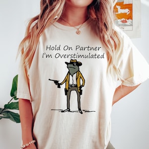 Comfort Colors® Hold On Partner Im Overstimulated Shirt Cowboy Frog T-Shirt | Funny Meme Shirt With Trending Quotes In Vintage Style
