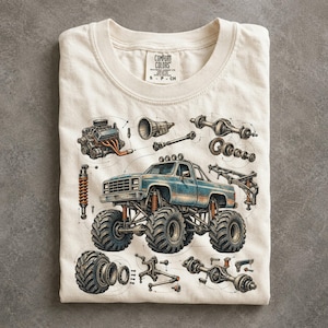 May include: A cream-colored t-shirt featuring a detailed graphic of a blue monster truck surrounded by various mechanical automotive parts, including an engine, transmission, axles, and suspension components, all rendered in a technical sketch style.