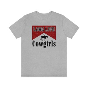 May include: A light gray t-shirt featuring a distressed red and white graphic with the words "LONG LIVE" above a silhouette of a person riding a horse, and the word "Cowgirls" below.
