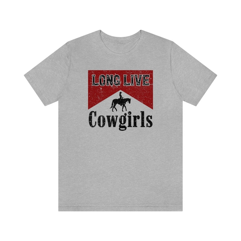 May include: A light gray t-shirt featuring a distressed red and white graphic with the words "LONG LIVE" above a silhouette of a person riding a horse, and the word "Cowgirls" below.