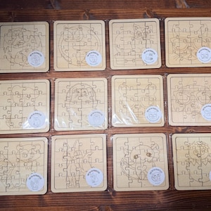 May include: Twelve square wooden jigsaw puzzles arranged in a grid, each featuring a unique laser-engraved animal illustration. The light-coloured wood puzzles are individually wrapped in clear plastic and include a small circular sticker on each.