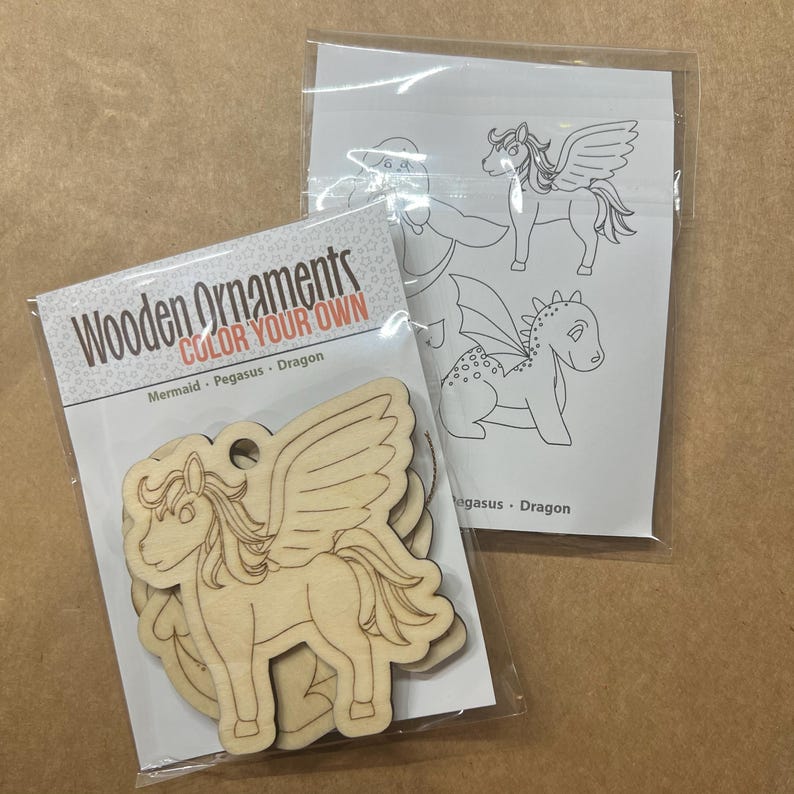 May include: A package of wooden ornaments in the shape of a pegasus. The ornaments are made of light-colored wood and are ready to be colored. The package also includes a sheet with line drawings of a pegasus and a dragon. The text on the package reads "Wooden Ornaments COLOR YOUR OWN".
