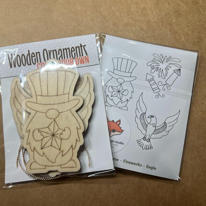 May include: Two packages of wooden ornaments. One package contains a wooden gnome-like figure with a top hat and star. The other package contains line drawings of a gnome, fireworks, and an eagle. The text "Wooden Ornaments" is visible.