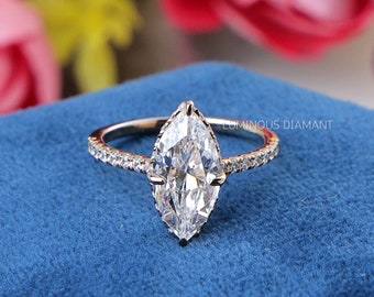 Könnte beinhalten: Ein silberner Ring mit einem Marquise-Diamanten in der Mitte und kleineren Diamanten, die in einer Pavé-Fassung um das Band herum gesetzt sind.