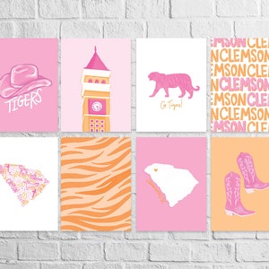 May include: A set of eight printable wall art prints featuring pink and orange designs. The prints include a pink cowboy hat with the word "Tigers" underneath, a pink tiger, a pink and orange striped pattern, a pink building with a clock tower, a white outline of the state of South Carolina with the words "South Carolina" underneath, a pink and orange striped pattern, a pink cowboy boot, and a pink and orange pattern with the words "Clemson" repeated.