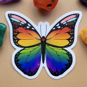 Peut inclure: Un autocollant de papillon arc-en-ciel avec un cristal vert, orange et violet à côté.