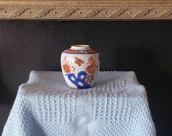 Peut inclure: Un vase en porcelaine bleu et blanc avec un motif floral posé sur une couverture bleu clair. Le vase a un corps rond et un col étroit.