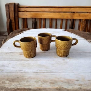 Könnte beinhalten: Drei braune Keramikbecher mit geometrischem Muster. Die Becher sind übereinander gestapelt.