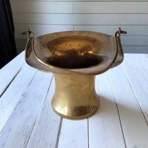 May include: A gold brass vase with a wide, flared opening and two handles. The vase has a smooth, polished finish.