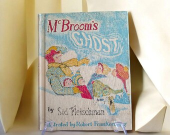 May include: A vintage children's book titled "McBroom's Ghost" by Sid Fleischman, illustrated by Robert Frankenberg. The cover shows a whimsical illustration of a family in winter clothing. The title is in red, with a light blue background.