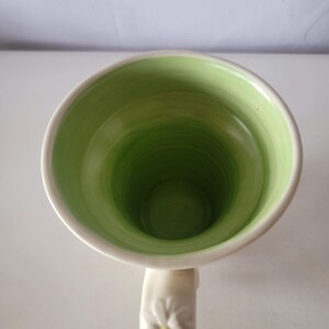 May include: A white ceramic mug with a green interior. The inside of the mug has a gradient of green hues, transitioning from light to dark. The handle is white and has a floral design.