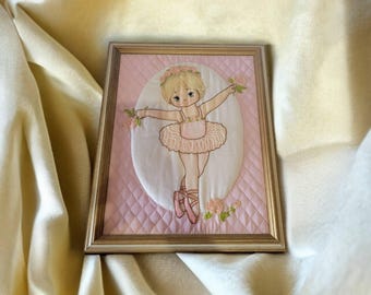 May include: A framed embroidered picture of a young girl dressed as a ballerina in a pink tutu and holding a flower. The background is pink with a quilted pattern.