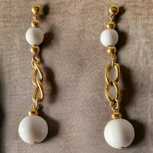 Puede incluir: Un par de pendientes colgantes de oro con cuentas de cerámica blanca y un diseño de cadena de eslabones de oro.