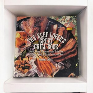 Op de afbeelding: Een kookboek met de titel "The Beef Lover's Great Grill Book" met een foto van gegrild vlees, groenten en wortelen op de omslag. Het boek is van Barbara Grunes.