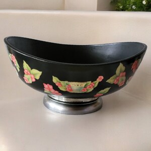 May include: Black oval serving bowl with a silver base and floral design. The bowl is decorated with pink and green flowers and leaves.