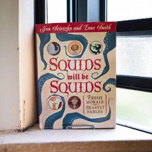 May include: A hardcover book titled "Squids Will Be Squids" by Jon Scieszka and Lane Smith. The cover features red lettering, blue tentacles, and cartoon illustrations. The book is propped up on a windowsill.