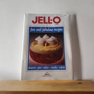 May include: A white cookbook with the title "JELL-O Fun and Fabulous Recipes" featuring a picture of a dessert with whipped cream and fruit.