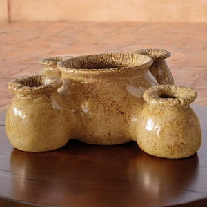 May include: A ceramic planter with four openings, each with a rounded, bulbous shape. The planter is a light brown color with a speckled glaze.