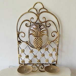 May include: Gold metal wall sconce with a pineapple design and a floral pattern. The sconce has two candle holders.