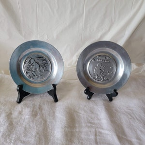 May include: Two silver plates with a raised design and text. The plate on the left says "Saturday's Child works hard for his living". The plate on the right says "Tuesday's Child is full of grace".