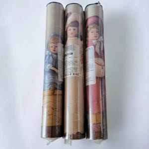 May include: Three rolls of wallpaper with a vintage children's theme. Each roll features a different illustration of a child in a dress, with a brown background and a white border. The text on the rolls reads "#855-9 R-02".