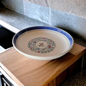 Puede incluir: Un bol de servir de cerámica blanca con un diseño floral azul y rojo. El bol está sobre una superficie de madera.