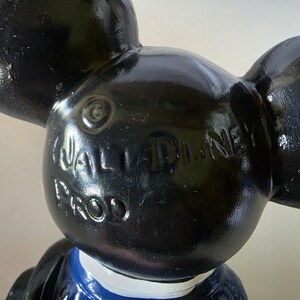 K&ouml;nnte beinhalten: Schwarze Mickey Mouse-Figur mit gro&szlig;en Ohren, schwarzem Kopf und blau-wei&szlig;em Outfit. Die Worte "WALT DISNEY PROD" sind auf dem Kopf gepr&auml;gt. Die Figur ist ein Sammlerst&uuml;ck.