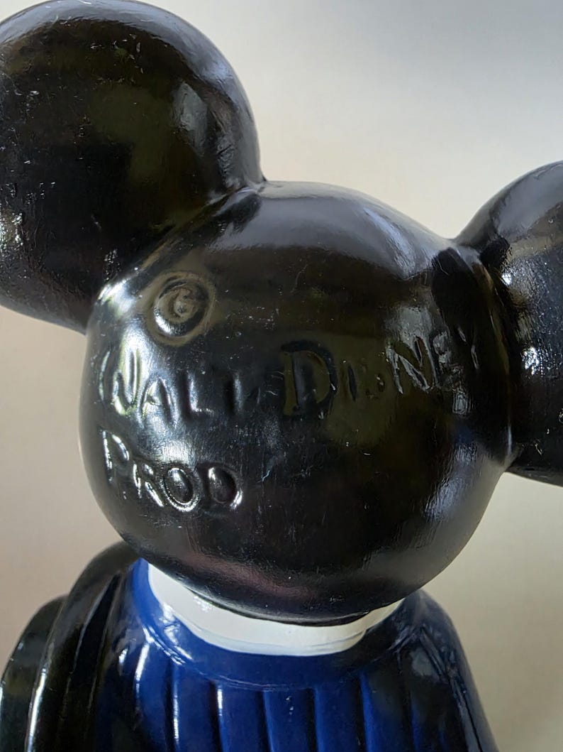K&ouml;nnte beinhalten: Schwarze Mickey Mouse-Figur mit gro&szlig;en Ohren, schwarzem Kopf und blau-wei&szlig;em Outfit. Die Worte "WALT DISNEY PROD" sind auf dem Kopf gepr&auml;gt. Die Figur ist ein Sammlerst&uuml;ck.