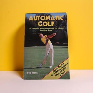 May include: A book titled "AUTOMATIC GOLF" with an image of a person swinging a golf club. The cover text reads "The Complete, Illustrated Method For Longer, Straighter Shots". A banner reads "Based On The Best-Selling Video - Over 400,000 SOLD!"