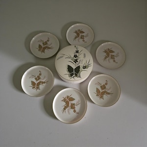 May include: A white ceramic mug with a black handle and the text "But First, Coffee" in a black, handwritten-style font. The mug is on a white surface.