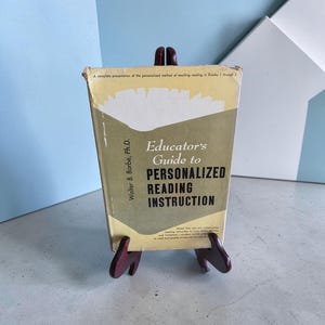 May include: A vintage hardcover book titled Educator's Guide to Personalized Reading Instruction by Walter B. Barbe, Ph.D. The cover features a pale yellow and olive green color scheme with black text and a stylized white graphic at the top.