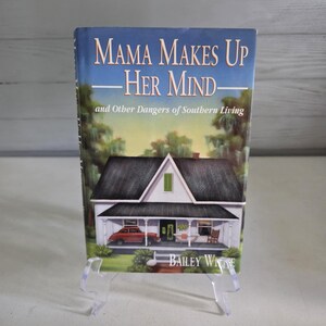 May include: A book titled "Mama Makes Up Her Mind" with the subtitle "and Other Dangers of Southern Living" is displayed. The cover features a watercolor illustration of a white house with a red car parked in front. The author's name, Bailey White, is visible.