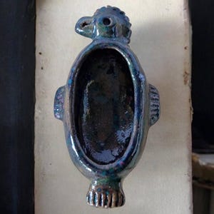 May include: A ceramic bird-shaped dish with a dark blue and green glaze. The dish has a hollow interior and a small opening on the top.