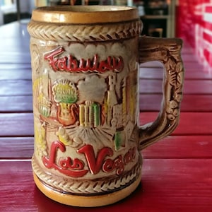 May include: A brown ceramic beer stein with a handle shaped like a vine. The stein has a colorful scene of a Las Vegas cityscape with the words "Fabulous Las Vegas" on the front.