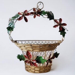 Peut inclure: Un panier en fil de fer doré avec une base tissée et une poignée décorée de fleurs de poinsettia rouges et vertes. Le panier est parfait pour contenir de petits objets ou à des fins décoratives.