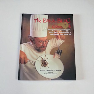 May include: A cookbook titled "The Eat-A-Bug Cookbook" featuring a chef holding a plate with a tarantula. The cover text includes "33 ways to cook grasshoppers, ants, water bugs, spiders, centipedes, and their kin."