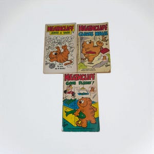 Peut inclure: Trois bandes dessinées vintage de Heathcliff. Les couvertures présentent le chat orange de dessin animé dans diverses situations, avec des titres tels que "Sins a Yarn", "Cleans Mouse" et "Gone Fishin'!" Les bandes dessinées ont un fond blanc.