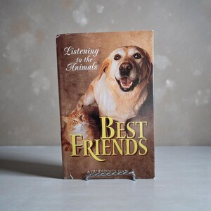 Könnte beinhalten: Buchcover mit einem Golden Retriever und einer orangefarbenen Katze. Der Titel "Best Friends" ist in goldenen Buchstaben geschrieben, mit "Listening to the Animals" darüber. Ein Guideposts-Buch.