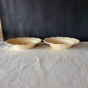 May include: Two large, cream-colored ceramic bowls with a decorative, raised floral design around the rim.