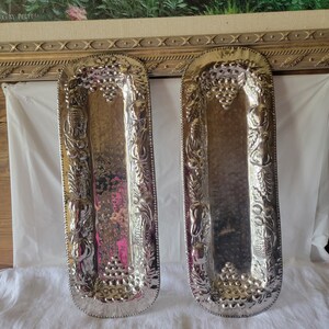 Puede incluir: Dos bandejas de servir plateadas con diseños grabados de uvas y flores. Las bandejas son rectangulares y tienen un acabado martillado.