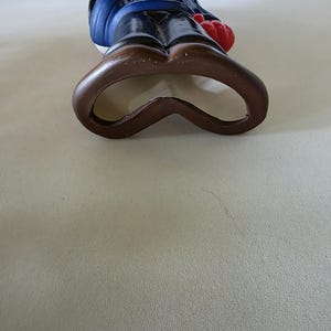 K&ouml;nnte beinhalten: Eine Flaschen&ouml;ffner-Figur von Micky Maus aus Keramik. Die Figur tr&auml;gt eine blaue Jacke, braune Hose und rote Handschuhe. Der Flaschen&ouml;ffner ist braun und hat die Form von Mickys Shorts.