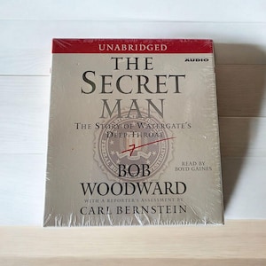 Puede incluir: Un audiolibro sellado titulado "The Secret Man" de Bob Woodward, que detalla el escándalo Watergate. La portada presenta el título en letras grandes y en negrita, con el subtítulo "The Story of Watergate's Deep Throat".